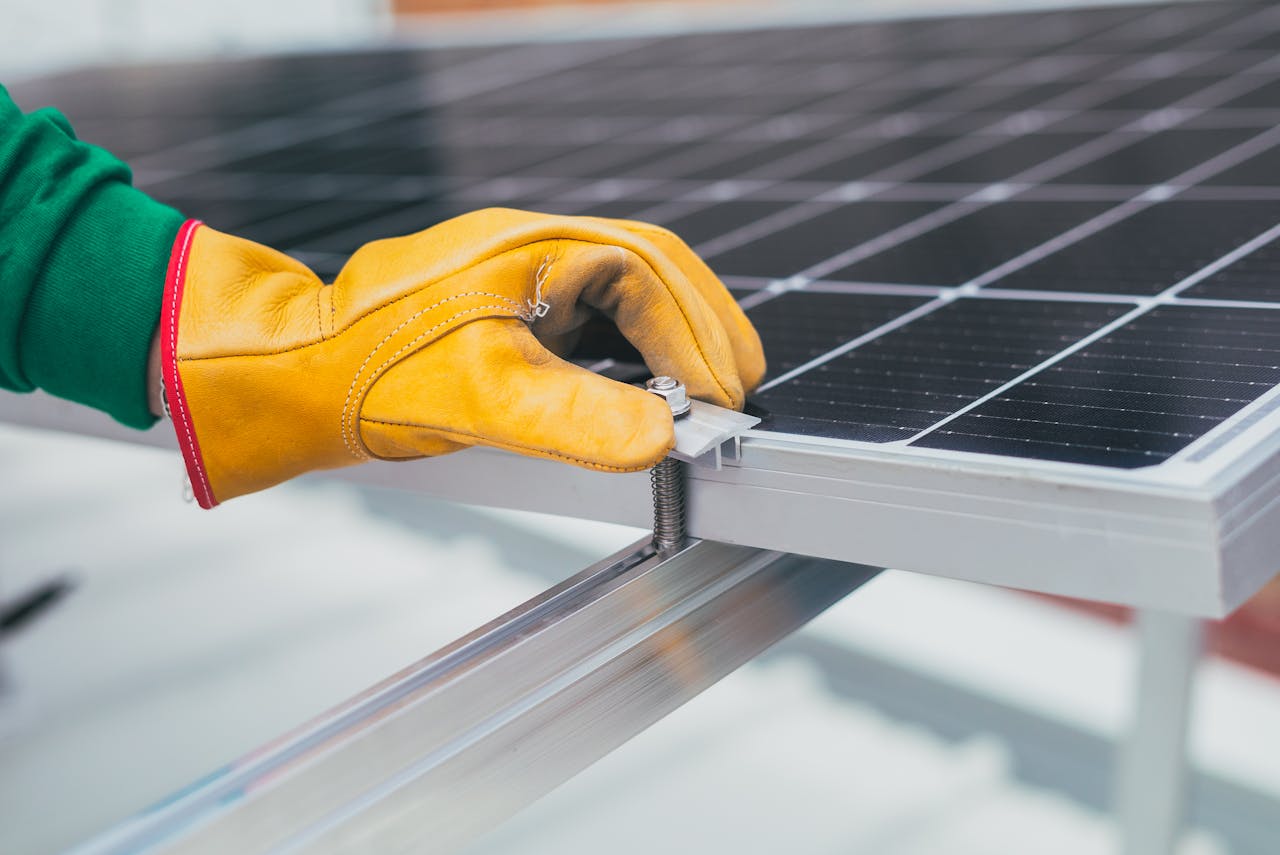 Close-up of a workers hand with protective gloves adjusting a bolt on a solar panel.